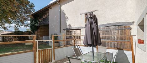 A patio with a glass table and chairs, surrounded by a wooden fence and a white wall.