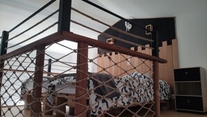 Un llit superposat amb estructura de fusta i xarxes de corda, un reposacapses negre i un petit moble prestatgeries.