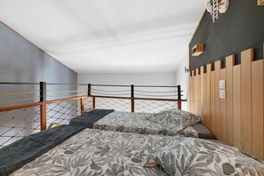 Une pièce comprenant un lit, une tête de lit en bois, une échelle en corde et un luminaire fixé au mur.