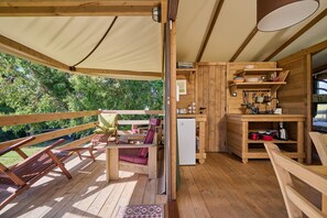 Eine Holzterrasse mit Liegestühlen, einer kleinen Küchenzeile mit Kühlschrank und einem Sonnensegel.