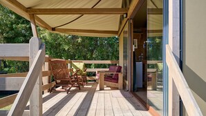 Un terrazzo in legno con mobili da esterno, una zona salotto coperta e una porta vetrata che dà su una stanza.