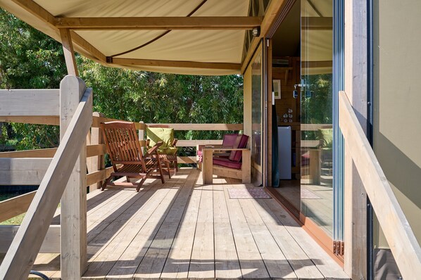 Eine Holzterrasse mit Gartenmöbeln, einem überdachten Sitzbereich und einer Glastür, die zu einem Raum führt.