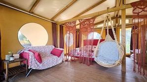 Une pièce avec un plancher en bois, un canapé agrémenté de coussins à motifs, un fauteuil suspendu et une petite table sur laquelle se trouve une radio.