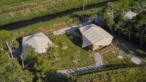 Une propriété rurale comprenant deux grands bâtiments aux toits blancs, entourés de verdure et bordée par une rivière.