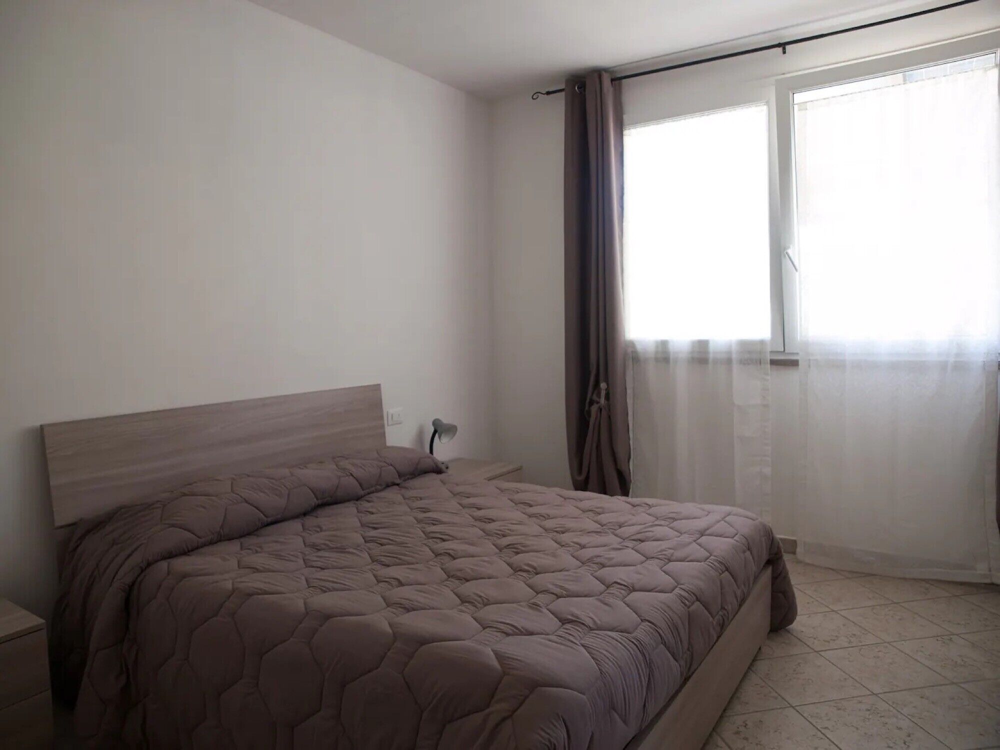 A bedroom with a bed, a nightstand, a lamp, and a window with curtains.