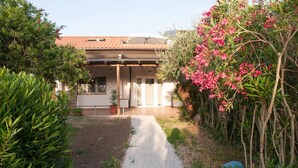 Un chemin menant à un bâtiment doté d’un toit en tuiles, entouré de verdure et de plantes en fleurs.