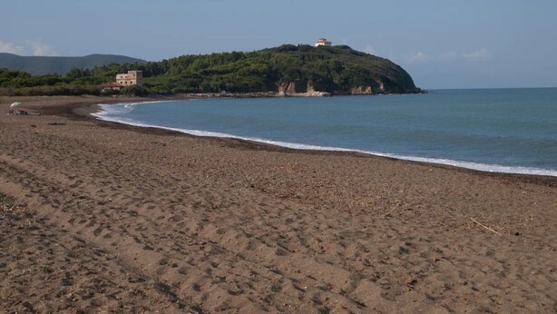 Une plage avec un bâtiment perché sur une colline, un ciel dégagé et une mer calme.