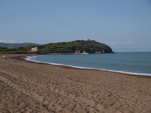 Une plage avec un bâtiment perché sur une colline, un ciel dégagé et une mer calme.