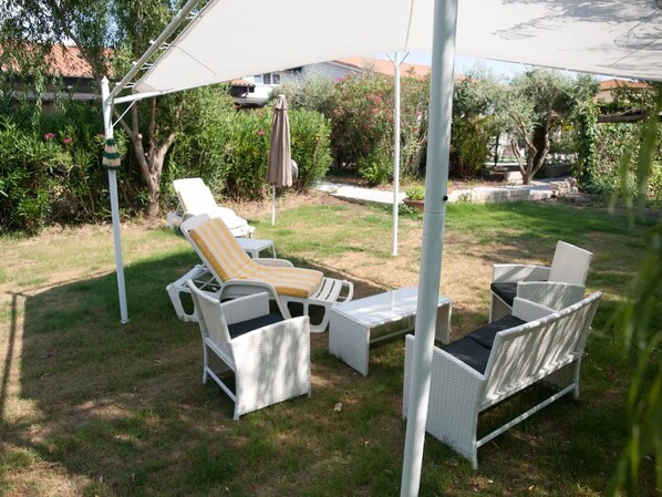 A patio with outdoor furniture, including a lounge chair and a sofa, under a white canopy.