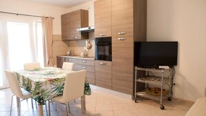 Une cuisine moderne avec des meubles en bois, une table à manger avec des chaises, un téléviseur et un petit chariot.