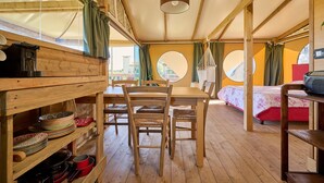 Ein Holzinnenraum mit Esstisch, Stühlen, einem Bett und einer Pendelleuchte.
