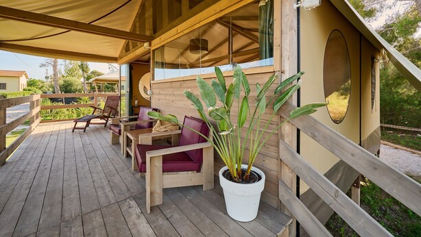 Eine Holzterrasse mit Sitzgelegenheiten im Freien, einem Blumentopf und einem überdachten Bereich mit einem Fenster.