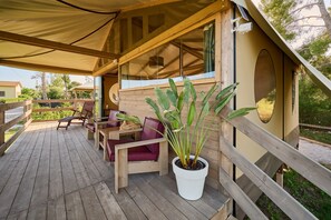 Una terraza de madera con mobiliario exterior, una planta en maceta y una zona cubierta con ventanal.