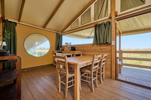 Una mesa de madera para comer con sillas, un espejo redondo y vistas al exterior a través de una ventana.