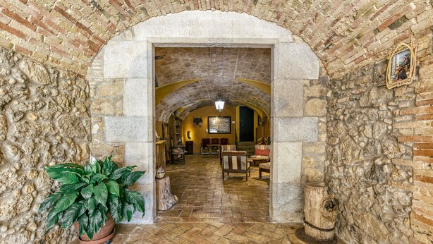 An arched stone corridor with a potted plant, rustic wooden furniture, and a stone wall with a decorative plate. - Farmhouse 'Mas Alba' with Mountain View, Private Pool and Wi-Fi (Terradelles Girona)