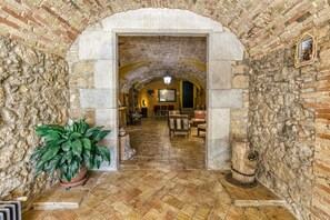 An arched stone corridor with a potted plant, rustic wooden furniture, and a stone wall with a decorative plate.