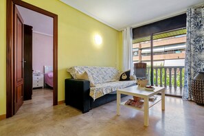 Una stanza con un divano, un tavolo, una porta e vista su un edificio attraverso una finestra.