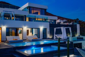 A modern hotel with a pool, lounge chairs, and a view of the mountains.