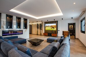 A modern living room with a sectional sofa, a flat-screen TV, built-in shelves, and a marble backsplash.