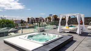 Ein Poolbereich auf dem Dach mit Whirlpool, Liegestühlen und Sonnensegel.