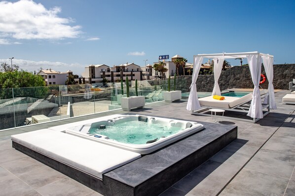 A rooftop pool area with a hot tub, lounge chairs, and a canopy.
