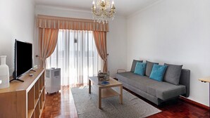 Un salon comprenant un canapé, un téléviseur, une table et un lustre.