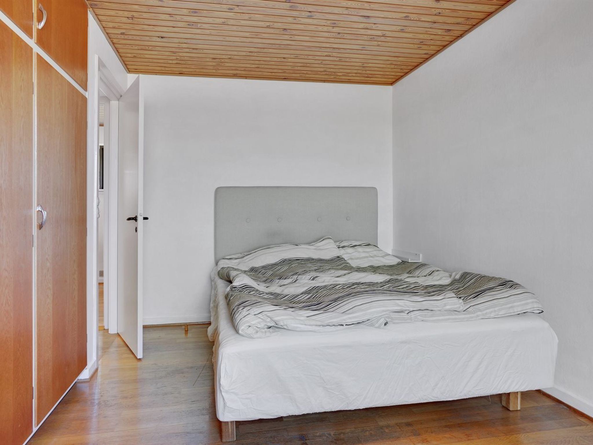 Ein Schlafzimmer mit Bett, Holzschrank und schrägverdeckter Decke.