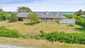 Uma casa de dois andares com telhado de metal, um quintal cercado e vista para o oceano.