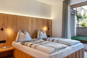 Ein modernes Schlafzimmer mit einem hölzernen Kopfteil, zwei Betten mit gestreifter Bettwäsche, Nachttischlampen und Blick auf einen Garten durch ein großes Fenster.