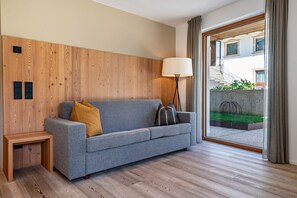 Ein modernes Wohnzimmer mit grauem Sofa, einer Wand aus Holzpaneelen, einer Stehlampe und Blick auf ein Gebäude durch eine Glastür.