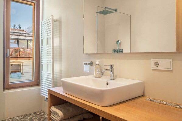 A bathroom with a large window, a white sink, a mirror, and a towel rack.