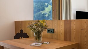 Ett träbord med en vas med blommor, ett tidningsnummer och en utsikt över en skog genom ett fönster.