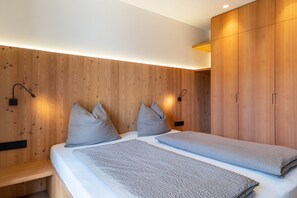 A modern bedroom with wooden panel walls, two beds with grey bedding, and built-in wardrobes.