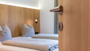 A wooden door with a modern handle, a keyhole, and a bed with a white mattress and pillows in the background. - Vista Dolomites Apartment "Harmony" with Mountain View, Private Garden & Wi-Fi (S. Cristina)