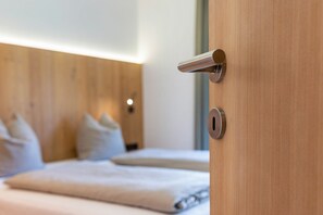 A wooden door with a modern handle, a keyhole, and a bed with a white mattress and pillows in the background.