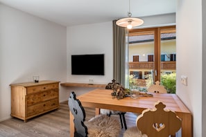 Un soggiorno moderno con un tavolo da pranzo in legno, una TV a parete e vista su un balcone con mobili da esterno.