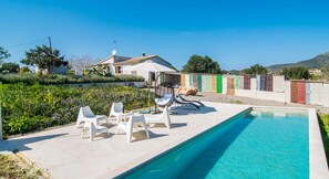 A swimming pool with a clear blue water, surrounded by white lounge chairs and a hanging chair.