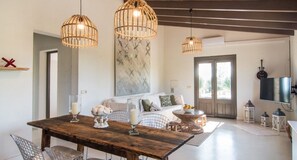 Un espace repas comprenant une table en bois, deux luminaires suspendus, un mur en marbre, un canapé et un téléviseur.