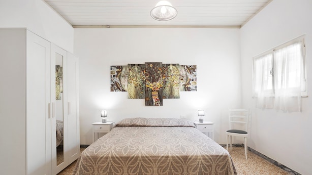 Un dormitorio con cama, mesita de noche, silla, armario y un cuadro abstracto grande en la pared.