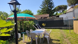 Un espacio de comedor al aire libre con una mesa, sillas, un farol y un paraguas verde.