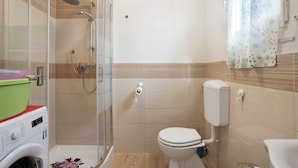 Un baño con ducha de vidrio, inodoro y lavadora.