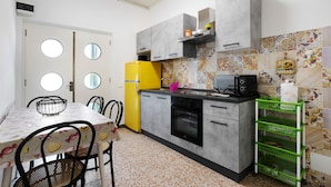 Una cocina con armarios grises, un refrigerador amarillo, un microondas y un estante de almacenamiento verde.