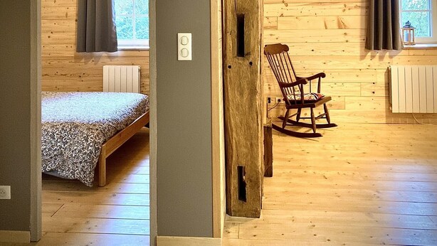 Un interior de madera con cama, mecedora y ventana con cortinas.