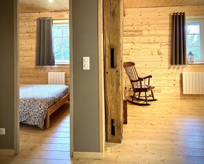 Un interior de madera con cama, mecedora y ventana con cortinas.