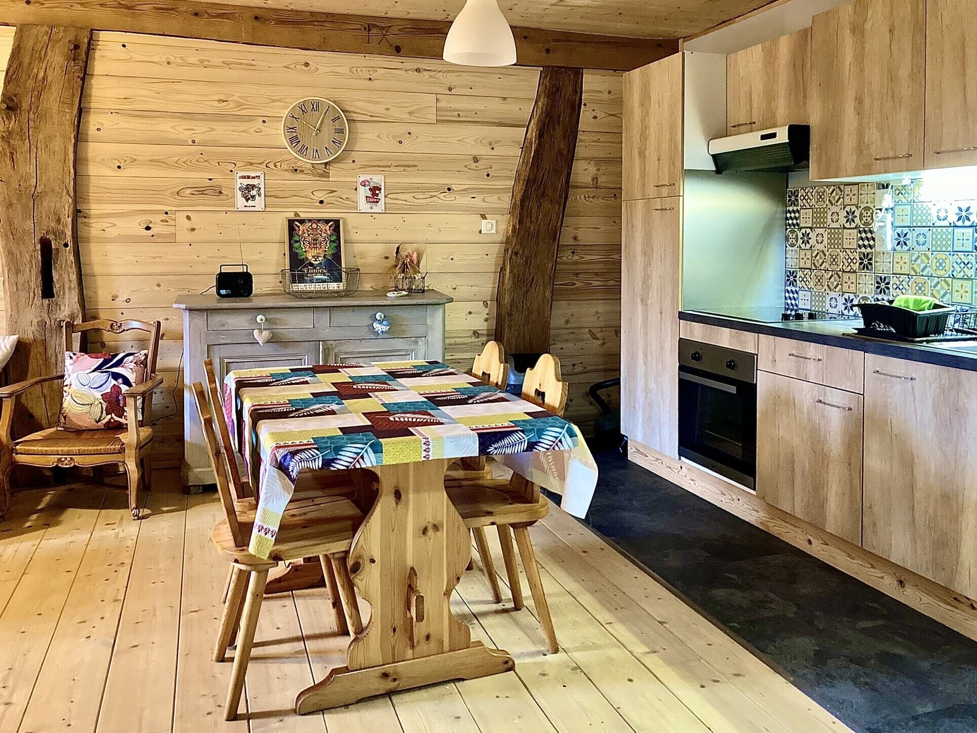 Un intérieur rustique en bois, avec une table à manger, des chaises, une horloge et un coin cuisine.