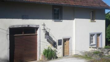 A building with a closed wooden garage door, a small entrance door, and a staircase leading to a second floor.