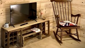 Una habitación con paneles de madera, un televisor sobre un soporte de madera, una mecedora y dos jaulas de pájaros colgadas en la pared.