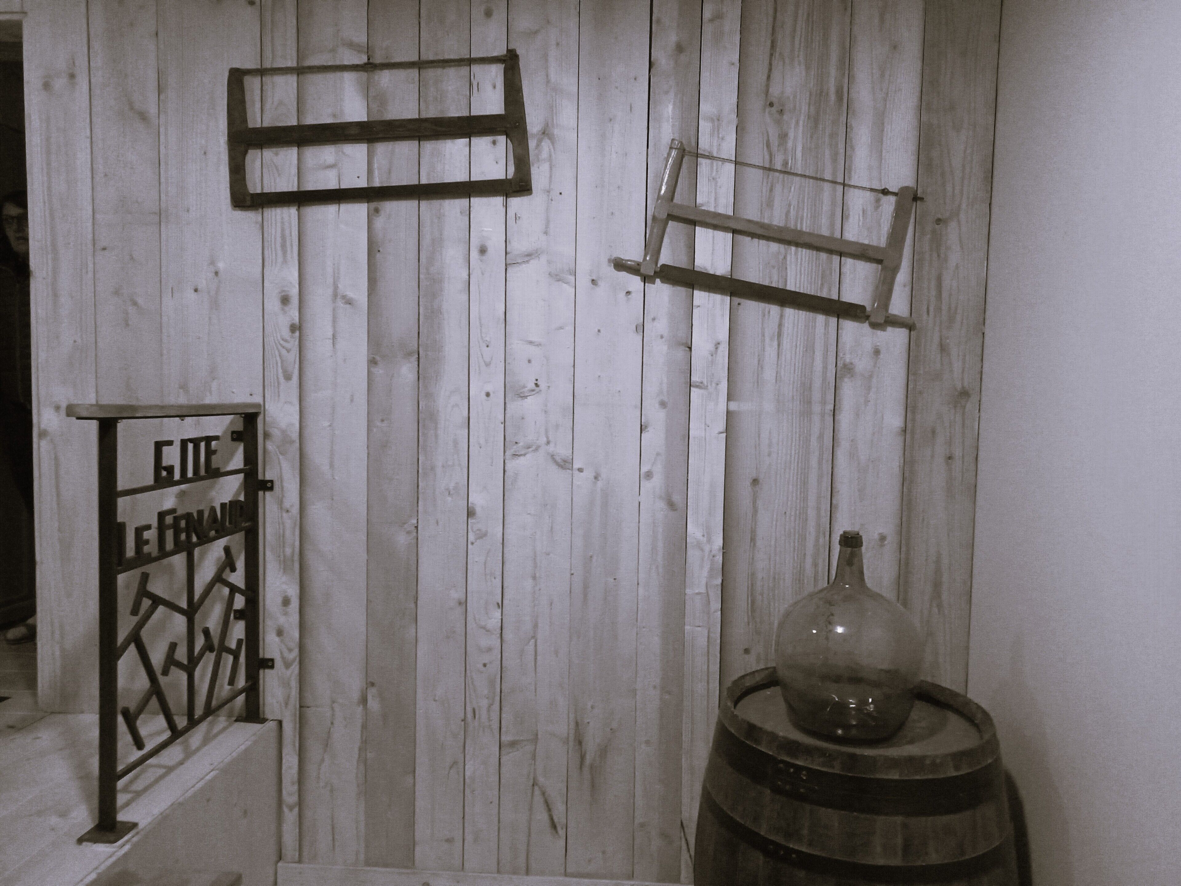 A rustic interior with wooden paneling, a metal gate labeled 'GITE LE FENAI,' and a barrel with a glass dome.