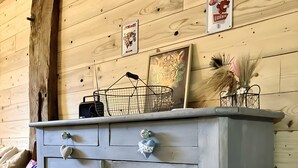 Un aparador de estilo vintage con dos cajones y un estante pequeño, ubicado frente a una pared de madera con un reloj y adornos decorativos.