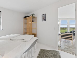 A bedroom with a bed, a wooden shelving unit, a framed picture, and a view of the outdoors.